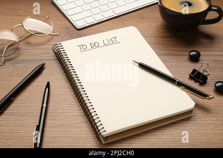 Notepad with inscription To Do List, pens, glasses and cup of coffee on wooden table Stock Photo