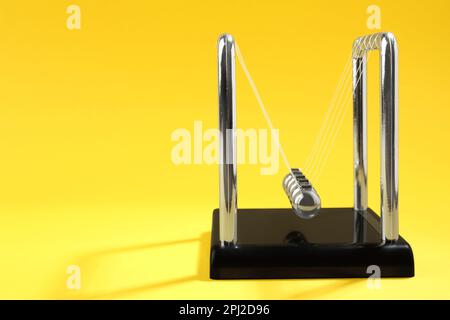 Newton's cradle on yellow background, space for text. Physics law of energy conservation Stock Photo