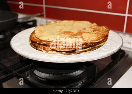Plate of freshly made crepes on stove in kitchen, closeup Stock Photo