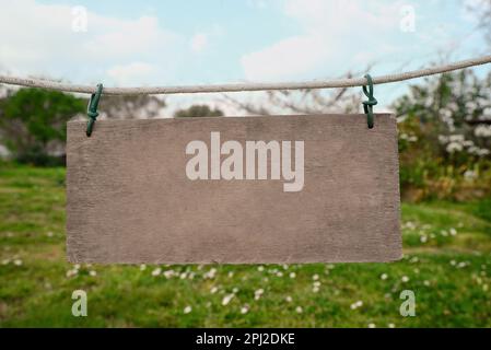Blank wooden board hanging on rope in countryside. Space for text Stock Photo