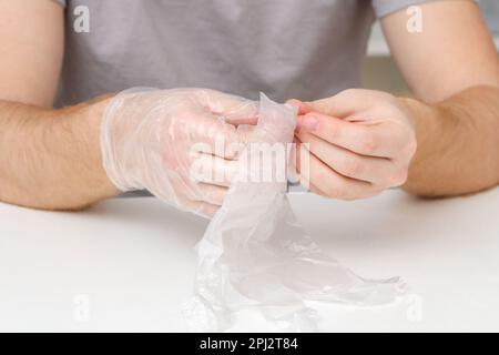 A man puts disposable plastic transparent gloves on his hands to dye Easter eggs. Coloring of Easter eggs. Stock Photo
