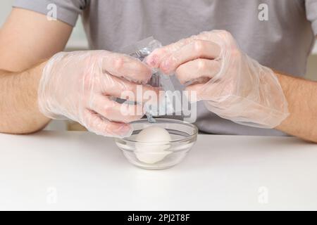 A man puts disposable plastic transparent gloves on his hands to dye Easter eggs. Coloring of Easter eggs. Stock Photo