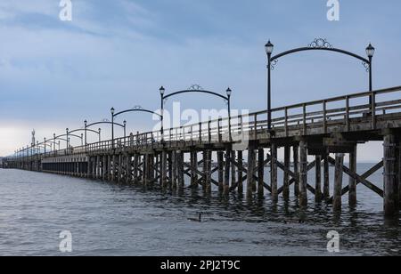 Wooden pier at White Rock, BC, Canada extends diagonally into image. Wooden Pier Walk during a cloudy sunset. Travel photo, selective focus Stock Photo