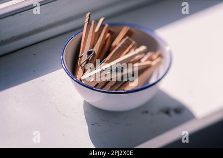old fashion wooden clothespins in blue rimmed enamel bowl sit on window shelf in bright sunlight Stock Photo