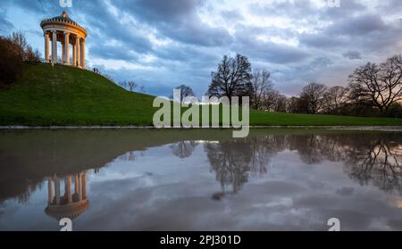 Munich, Germany. 30th Mar, 2023. The Monopteros is reflected in a puddle in the English Garden at sunset. The German Weather Service forecasts cloudy and rainy weather for Friday. This is not expected to change towards the weekend. Credit: Peter Kneffel/dpa/Alamy Live News Stock Photo