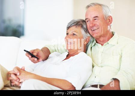 Relaxed couple watching television. Relaxed mature couple watching television while sitting on couch. Stock Photo