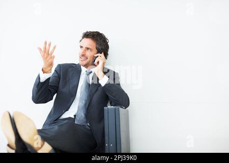 Handsome executive talking on cellphone. Handsome executive sitting against wall and talking on cellphone. Stock Photo
