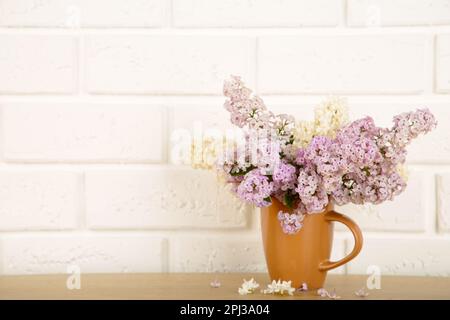 Room interior with purple lilacs flower blossom in tea cup on table, romantic spring home decor. Stock Photo