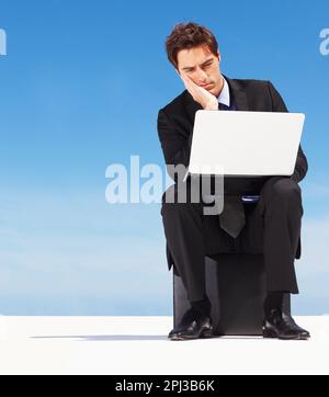 Worried business man looking at laptop against blue sky. Portrait of a worried young business man looking at laptop against natural background. Stock Photo