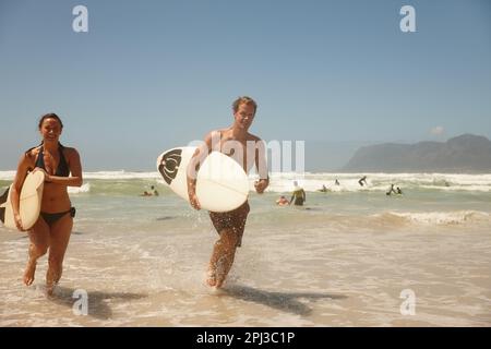 Doing what they love over the weekend. a couple surfing together at their favourite beach. Stock Photo