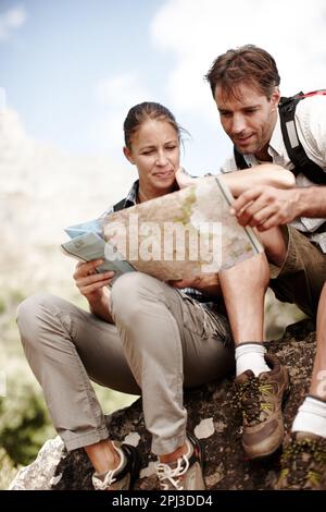 Checking their next route. Two hikers consulting their map while sitting on a mountain top. Stock Photo