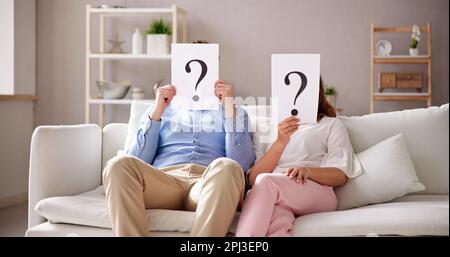 Couple Sitting On Sofa Holding Question Mark Sign In Front Of Face Stock Photo