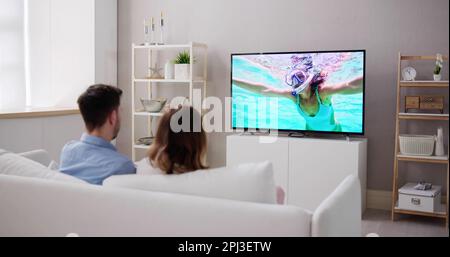 Young Couple Sitting On Couch Watching Television Show Stock Photo