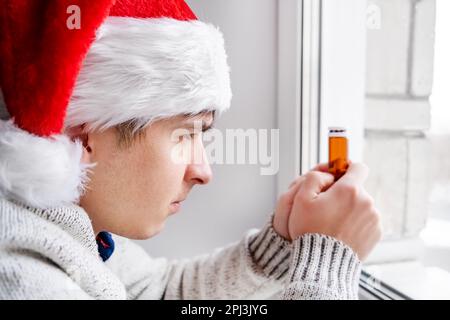 Young Man in Santa's Hat hold a Pills by the Window in the Room Stock Photo