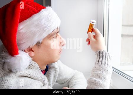 Young Man in Santa Hat with a Pills by the Window in the Room Stock Photo