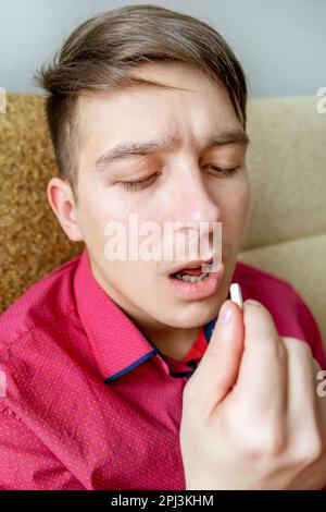 Sick Young Man take a Pill on the Sofa at the Home closeup Stock Photo