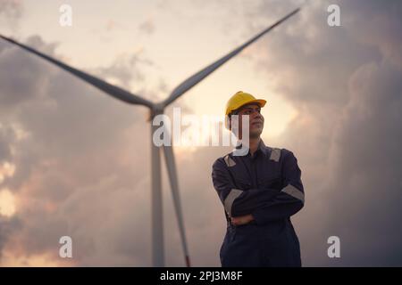 Happy young engineer in uniform with standing in wind turbine farm field. Stock Photo
