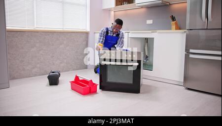 Young Male Repairman Repairing Oven In Kitchen Stock Photo