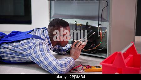 Young Male Serviceman Working On Fridge With Screwdriver At Home Stock Photo
