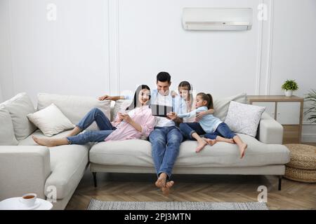Happy family resting under air conditioner on white wall at home Stock Photo