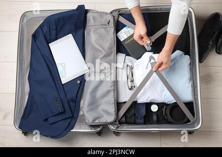 Man packing suitcase for business trip on wooden floor, top view Stock Photo
