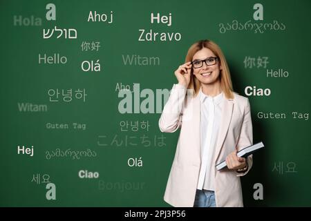 Portrait of happy translator and greeting words in different foreign languages on green background Stock Photo