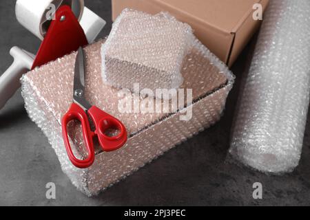 Cardboard boxes, bubble wrap, adhesive tape and scissors on dark grey table Stock Photo