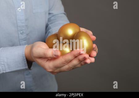 Woman holding shiny golden eggs on grey background, closeup Stock Photo