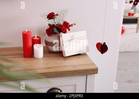 Vase with beautiful flowers, gift box and candles on wooden table indoors. Happy Valentine's Day Stock Photo