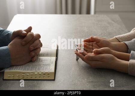 Boy praying and reading Bible with his godparents at grey table indoors, closeup Stock Photo