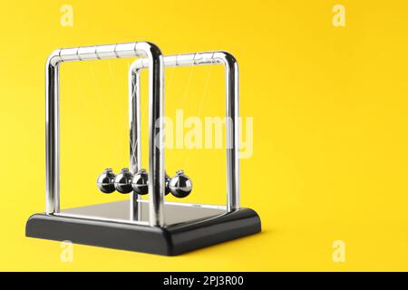 Newton's cradle on yellow background, space for text. Physics law of energy conservation Stock Photo