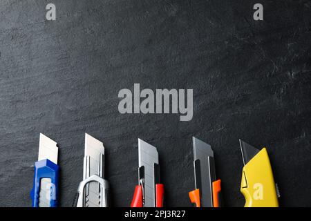 Different utility knives on black table, flat lay. Space for text Stock Photo