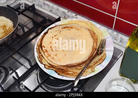 Plate of freshly made crepes with fork on stove in kitchen Stock Photo