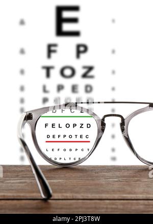 Glasses on wooden table. View through lenses on eye chart, white background Stock Photo