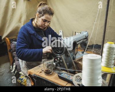 Fez, Morocco - January 07, 2020: Unknown young woman working with sewing machine, mending clothes to be sold at her market stall Stock Photo