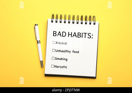 Notebook with list of bad habits and pen on yellow background, top view. Change your lifestyle Stock Photo