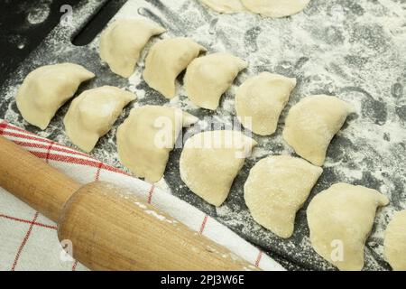 The process of making dumplings from dough. Traditional homemade food. Dough for dumplings. Raw dumplings on a wooden board. The process of making dum Stock Photo