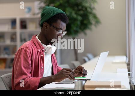 Focused black hipster guy remote online works on laptop typing on keyboard in coworking office space Stock Photo