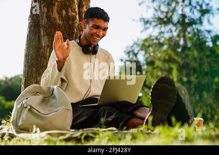 Young black man smiling and using laptop while sitting under tree in park Stock Photo