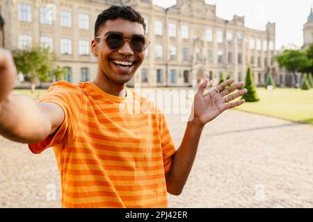 Young black man wearing piercing and sunglasses gesturing while taking selfie photo outdoors Stock Photo