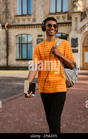 Young black man with headphones and backpack walking by college outdoors Stock Photo