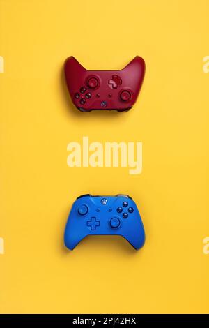 Two wireless gamepads red and blue lie on a yellow background.  Confrontation of players, battle in the game online Stock Photo