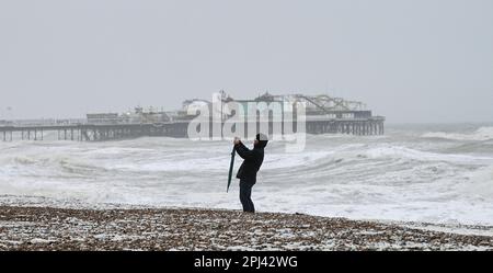 Brighton UK 31st March 2023 - A walker stops to take photographs on Brighton beach early this morning as Storm Mathis batters  the South Coast today with winds forecast to reach 70mph in some areas : Credit Simon Dack / Alamy Live News Stock Photo