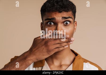 Shocked black man covering his mouth and looking at camera isolated over beige background Stock Photo