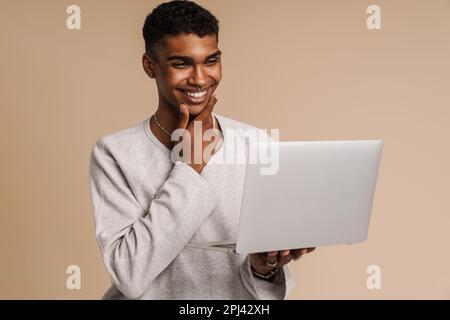 Young black man smiling while working with laptop isolated over beige background Stock Photo