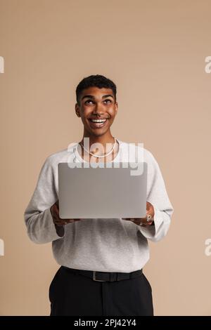 Young black man smiling while working with laptop isolated over beige background Stock Photo