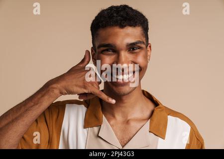 Young handsome smiling happy african man with piercing doing phone gesture with hand and fingers and looking at camera, while standing over isolated b Stock Photo