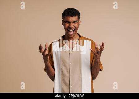 Young handsome insidious african man with piercing with raised hands and opened mouth looking at camera, while standing over isolated orange backgroun Stock Photo