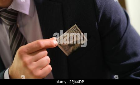 Businessman in business suit pulling out hundred dollar bill from pocket closeup Stock Photo