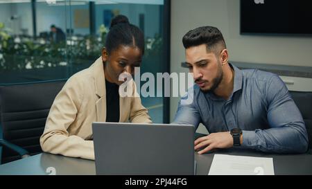 Diverse Indian Arabian man and African American woman colleagues discuss financial data analyzing documents marketing project result in report use Stock Photo